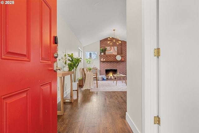 foyer entrance featuring vaulted ceiling, a brick fireplace, dark wood finished floors, and baseboards