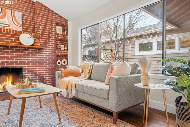 living room with lofted ceiling, brick wall, a brick fireplace, and wood finished floors