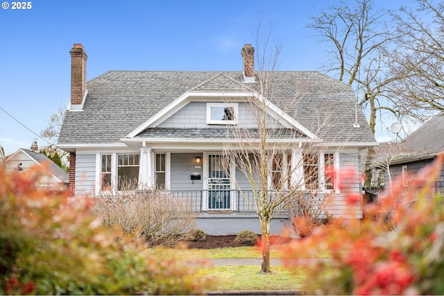 view of front of home with covered porch, roof with shingles, and a chimney