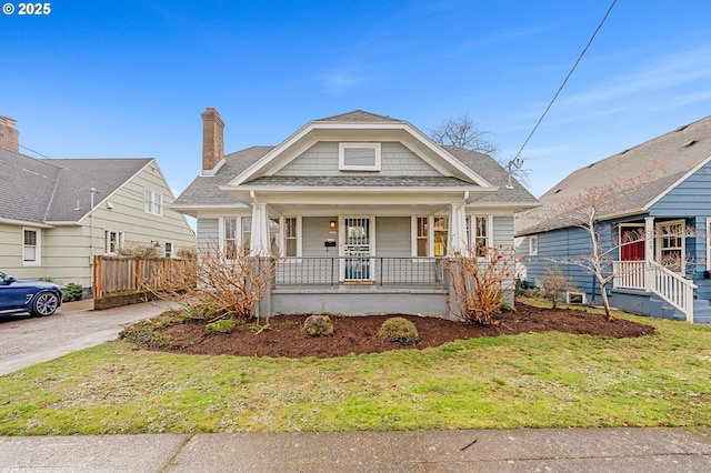 view of front of house with covered porch, a front lawn, a shingled roof, and fence