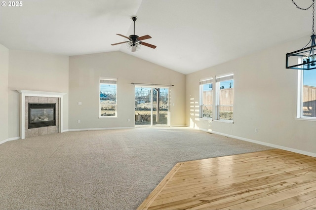 unfurnished living room featuring a tile fireplace, ceiling fan with notable chandelier, light carpet, and lofted ceiling