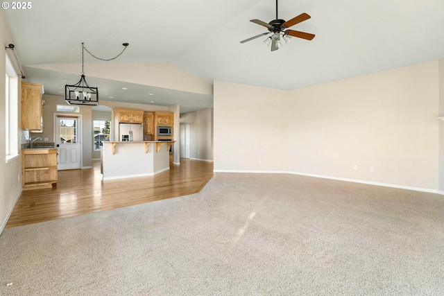 unfurnished living room featuring lofted ceiling, sink, ceiling fan with notable chandelier, and light carpet