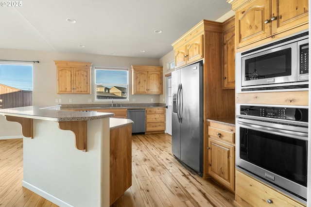 kitchen with light hardwood / wood-style floors, a kitchen breakfast bar, a center island, and appliances with stainless steel finishes