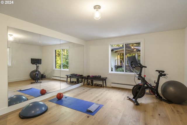 exercise area featuring baseboards, a baseboard heating unit, and wood finished floors