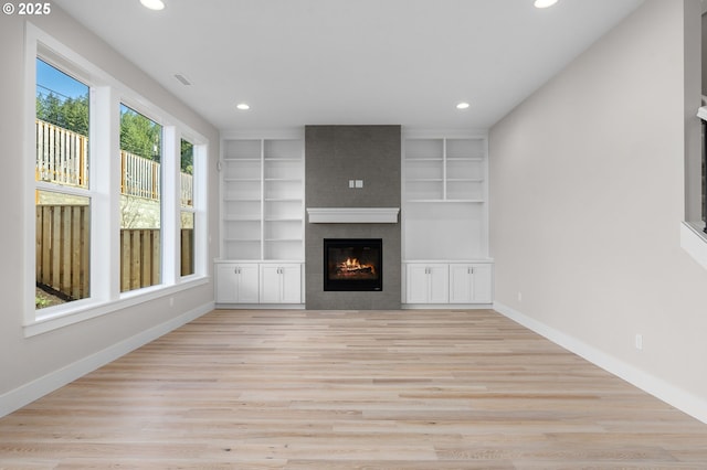 unfurnished living room featuring built in shelves, a large fireplace, and light wood-type flooring