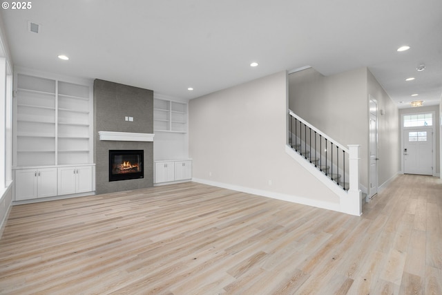 unfurnished living room with built in shelves, a large fireplace, and light hardwood / wood-style flooring