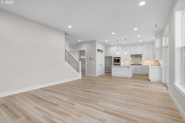 kitchen featuring white cabinetry, hanging light fixtures, a kitchen island, decorative backsplash, and stainless steel oven