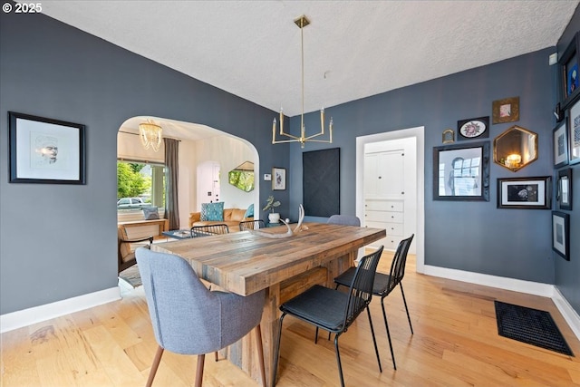 dining room with arched walkways, a chandelier, light wood finished floors, and baseboards