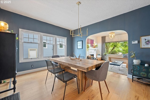 dining space with arched walkways, light wood finished floors, a chandelier, and a textured ceiling