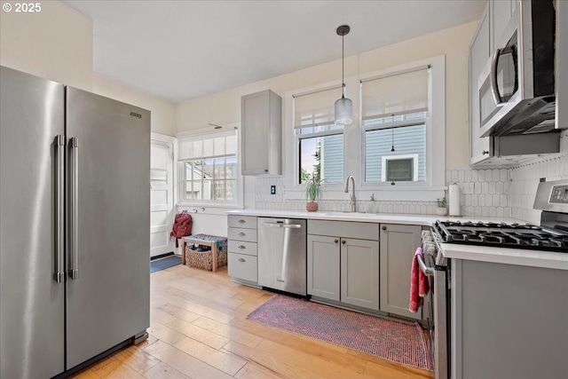 kitchen with appliances with stainless steel finishes, gray cabinetry, a sink, and light wood-type flooring