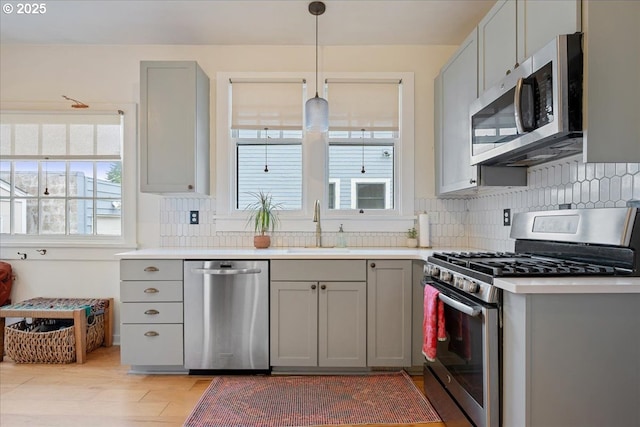 kitchen with appliances with stainless steel finishes, gray cabinetry, a sink, and backsplash