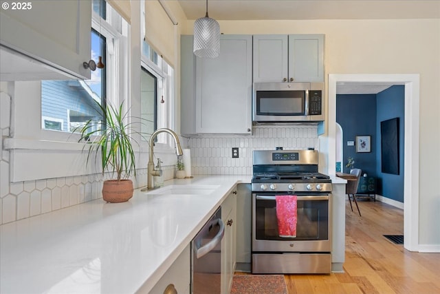 kitchen featuring appliances with stainless steel finishes, a sink, light countertops, light wood-style floors, and decorative backsplash