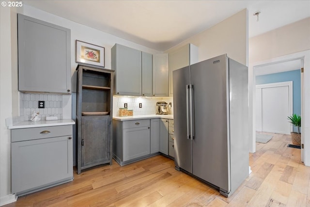 kitchen featuring high quality fridge, gray cabinetry, light countertops, backsplash, and light wood-style floors