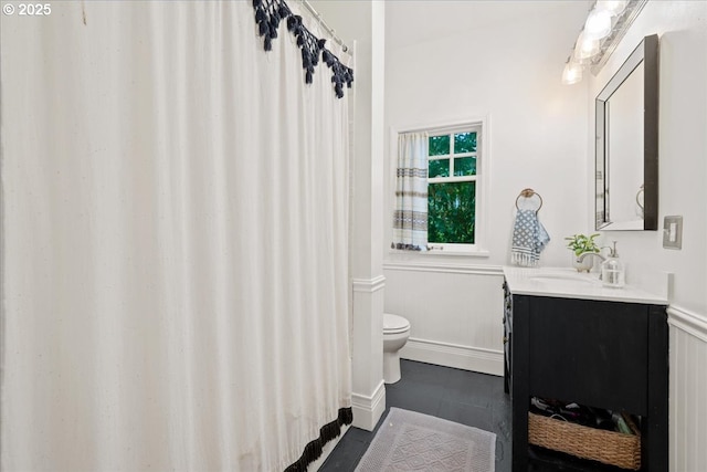 full bathroom featuring toilet, vanity, a wainscoted wall, and a shower with shower curtain
