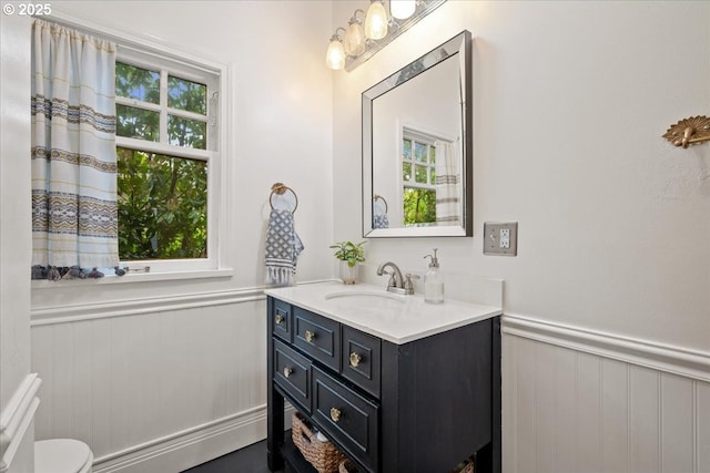 half bathroom featuring a wainscoted wall, vanity, and toilet