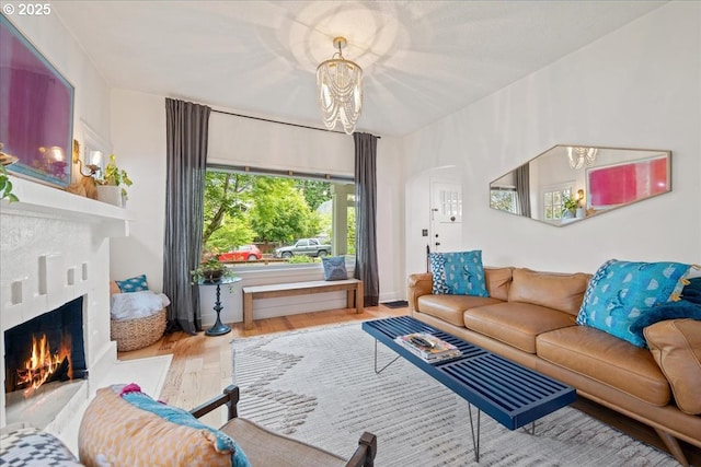 living room featuring wood finished floors, a lit fireplace, a chandelier, and arched walkways