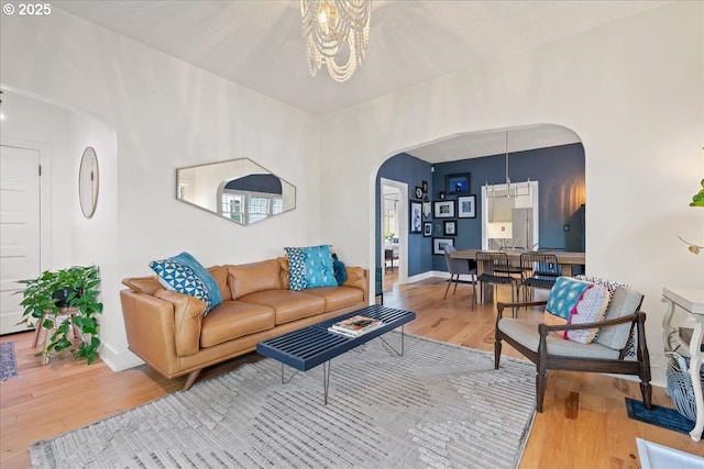 living room featuring arched walkways, wood finished floors, a chandelier, and baseboards