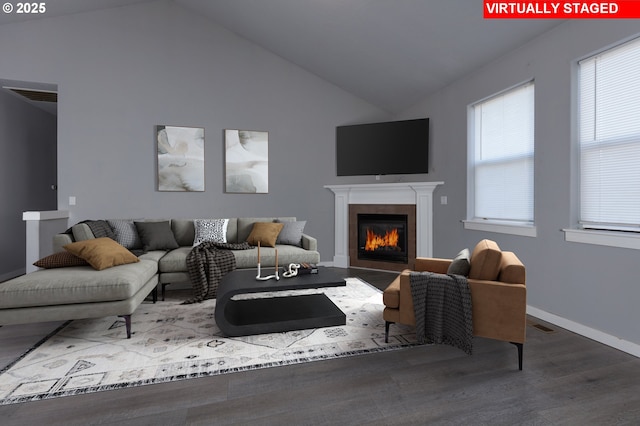 living area featuring visible vents, baseboards, a glass covered fireplace, lofted ceiling, and wood finished floors