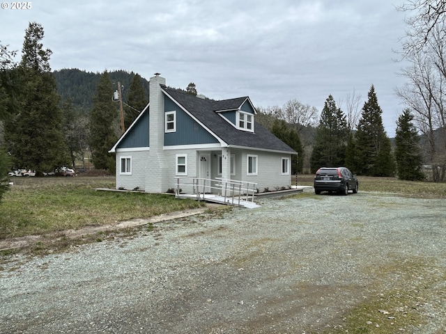 view of front of home featuring driveway, a forest view, a chimney, and a front yard