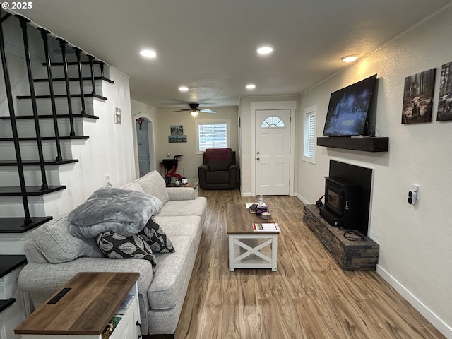 living area featuring baseboards, arched walkways, wood finished floors, a wood stove, and recessed lighting