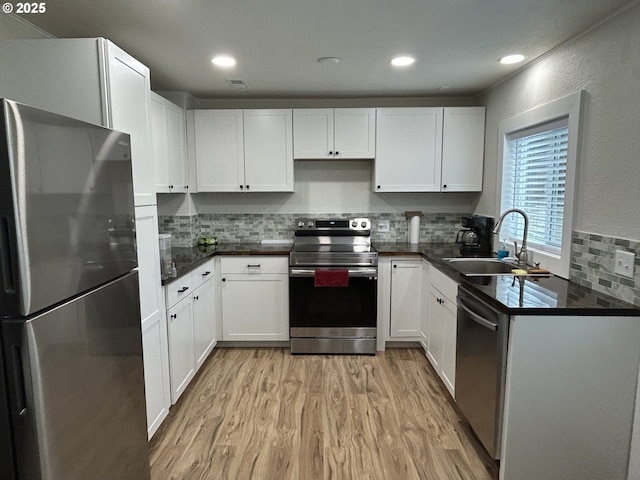 kitchen with stainless steel appliances, dark countertops, a sink, and white cabinets