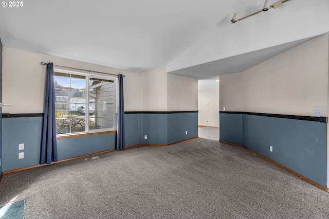 carpeted empty room with visible vents, vaulted ceiling, and baseboards