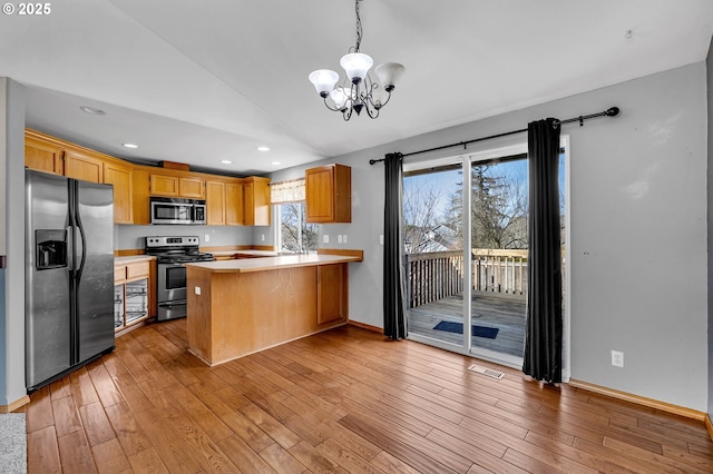 kitchen featuring lofted ceiling, light wood-style flooring, stainless steel appliances, a peninsula, and light countertops