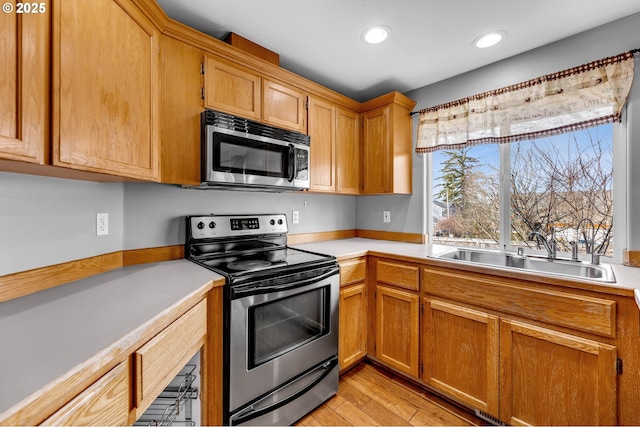 kitchen featuring appliances with stainless steel finishes, light countertops, a sink, and light wood-style flooring