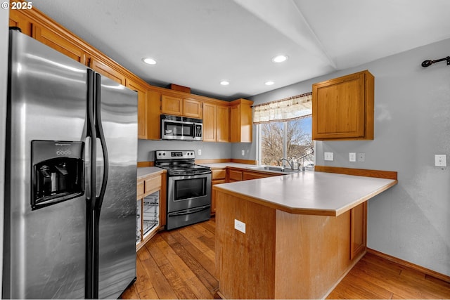 kitchen with stainless steel appliances, light countertops, light wood-style floors, a sink, and a peninsula