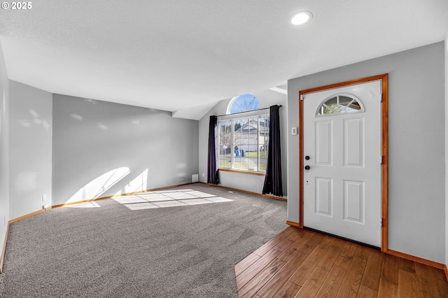 foyer entrance with lofted ceiling, carpet, baseboards, and wood finished floors