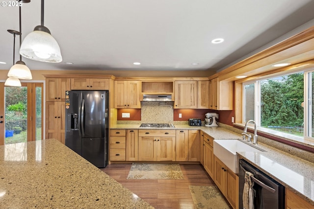 kitchen featuring hanging light fixtures, light stone countertops, under cabinet range hood, black appliances, and a sink