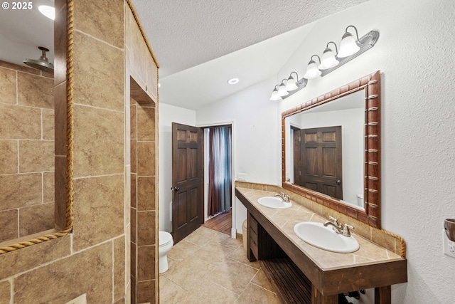 full bath featuring double vanity, toilet, vaulted ceiling, a textured ceiling, and a sink