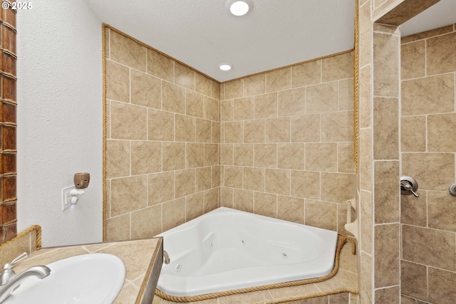 full bath featuring recessed lighting, a sink, a textured ceiling, and a tub with jets