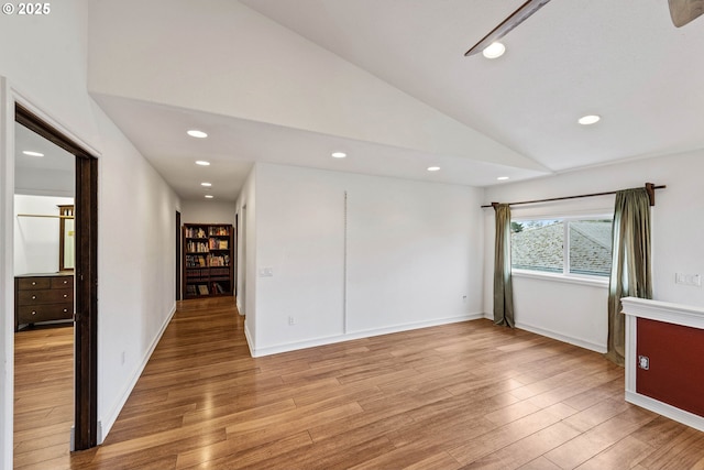 empty room featuring lofted ceiling, light wood-type flooring, baseboards, and recessed lighting