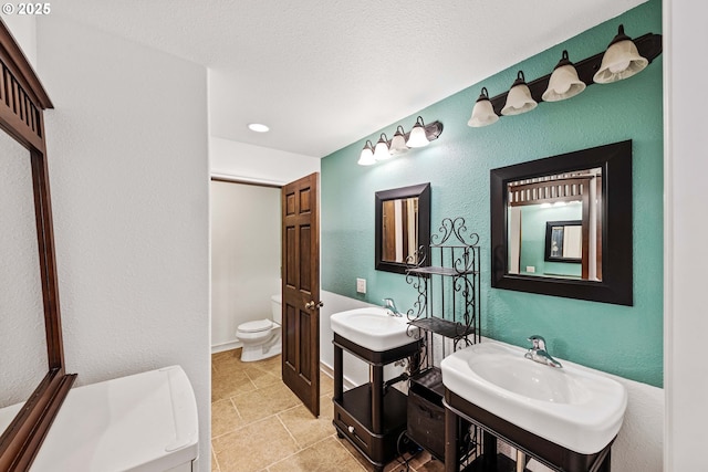 bathroom with toilet, a textured ceiling, two sinks, and a textured wall