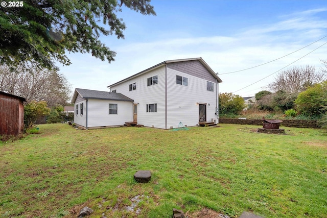 rear view of house featuring entry steps, a yard, and a fire pit