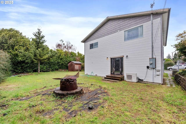 rear view of property featuring entry steps, a storage shed, a fire pit, an outdoor structure, and a lawn