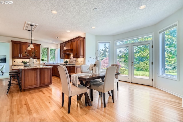 dining space featuring light wood-style floors, recessed lighting, a textured ceiling, and a healthy amount of sunlight