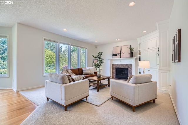 living area featuring light wood-style floors, a fireplace, a textured ceiling, recessed lighting, and baseboards