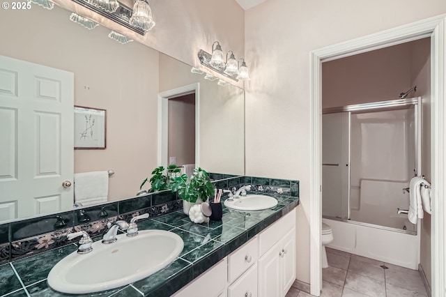 full bath with double vanity, a sink, combined bath / shower with glass door, and toilet
