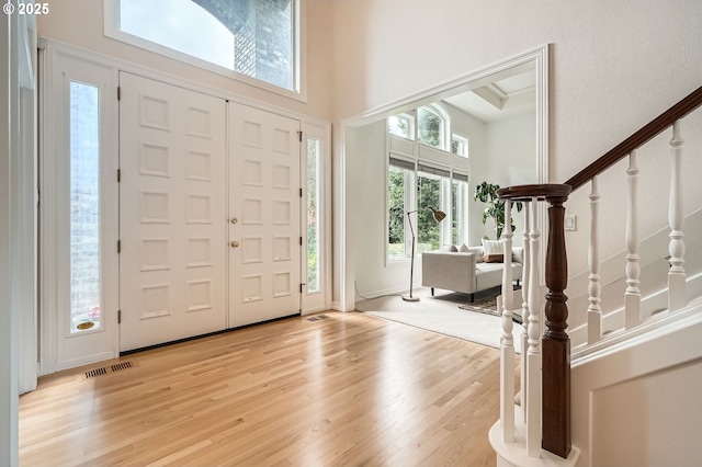 entryway with light wood-type flooring, stairs, a towering ceiling, and visible vents