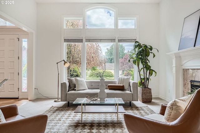 living area with a fireplace, a wealth of natural light, carpet, and a towering ceiling