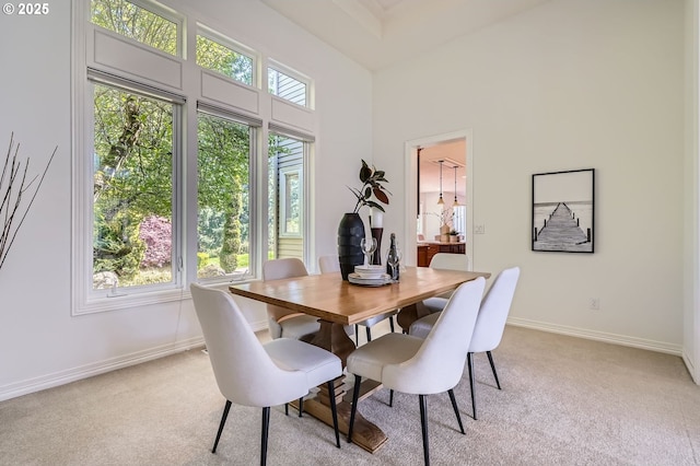 dining space featuring baseboards, light carpet, and a towering ceiling