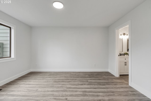 unfurnished bedroom featuring ensuite bath, wood finished floors, and baseboards