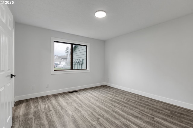 unfurnished room featuring visible vents, a textured ceiling, baseboards, and wood finished floors