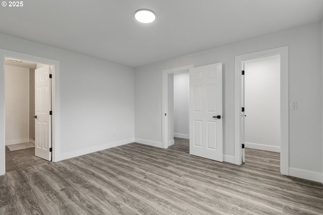 unfurnished bedroom with a spacious closet, wood finished floors, and baseboards