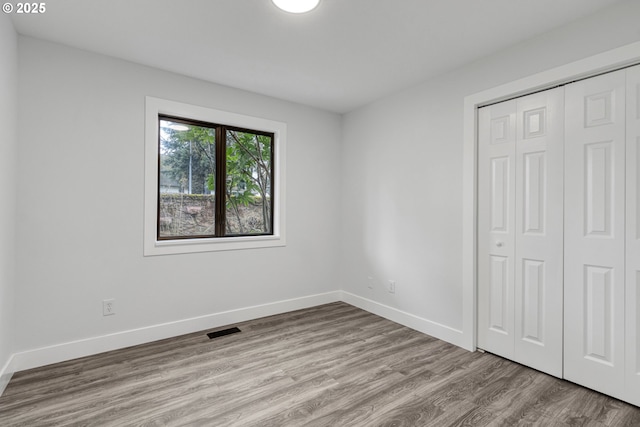 unfurnished bedroom with a closet, visible vents, baseboards, and wood finished floors