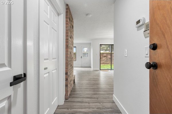 hallway with a textured ceiling, baseboards, and wood finished floors