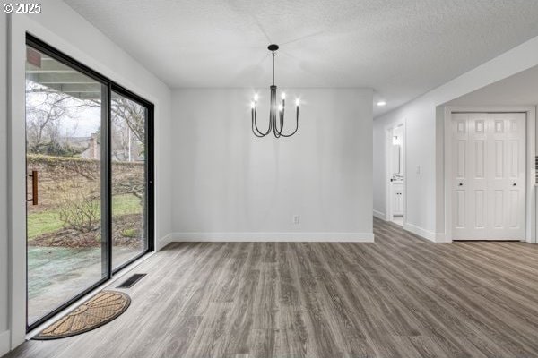 unfurnished dining area featuring a chandelier, wood finished floors, visible vents, and baseboards