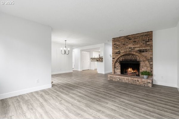 unfurnished living room with baseboards, a fireplace, wood finished floors, and an inviting chandelier